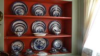 Full display of Royal Doulton Majestic Collection fine china items arranged on a red painted shelf including dinner plates, bowls, cups, saucers, sugar bowl, creamer, and serving bowl.
