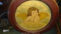 Front view of large round wood framed hand painted cherub with text