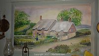 Full view of thatched cottage oil painting on board with decorative lamps on display