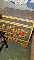 Close view of the front corner showing floral painted decoration and side handle.
