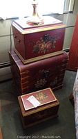 Front and slightly angled view of the three wooden painted chests stacked: largest at bottom, medium in middle, smallest on top, showing floral hand-painted details and metal hardware.