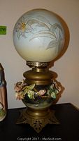 Full view of vintage Majolica table lamp with brass base, floral ceramic body with broken leaves, and frosted glass globe shade with painted flowers.