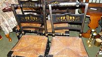 Overhead view of 4 black painted Hitchcock style chairs with gold stenciling and rush seats, showing wear and scratches to paint.