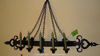 Photo of black metal hammered wall candelabra with chains and six green candles mounted on a wall.