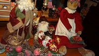 Large Santa and assorted Christmas figurines and ornaments on a table with pine cones visible
