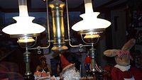 Full view of the hanging vintage reproduction ceiling lamp with two glass shades and brass fittings; surrounded by decorative figurines.