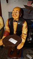Front view of the grandpa butler statue holding a round tray, showing detailed facial features including glasses and a bow tie.