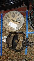 Cast iron bell and Rowe Pottery sundial visible side by side from the top, showing the bell's clapper and sundial's face with Roman numerals and leaf designs.