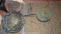 Cast iron hanging basket next to a round floor grate and cast iron lantern lid with floral decoration and chain