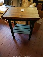 Full view of the butcher's block island kit table with green painted legs and bottom shelf, wooden top showing wear.