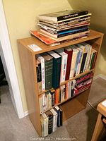 Image of wood bookshelf filled with assorted books on shelves and additional books stacked on top
