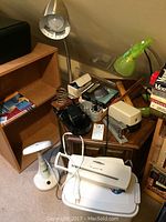 Desk with various office items including three desk lamps, vintage stapler, wooden side table, paper shredder, rulers, and boxed office supplies.