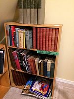 Wooden bookshelf filled with multiple books of varied sizes and colors including a known classic set on the top shelf.