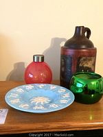 Four decorative items including a clay pot with Mona Lisa image, a red flower pot, green flower pot, and zodiac bowl on wooden surface