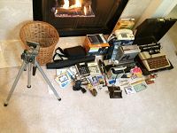 Wide shot showing entire lot with cameras, binoculars, typewriter, phones, tripod and various office supplies on carpet in front of fireplace.