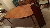 Photo showing solid wood dining table with one leaf detached and standing upright beside the table.