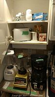 Photo of shelf and countertop showing Black & Decker coffee maker, two Osterizer blenders with different bases, white toaster, and Black & Decker carving knife in box.