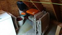 Photo showing patio loungers folded and leaning against a wall along with the plastic shelf and plant pots under a slanted wooden roof.