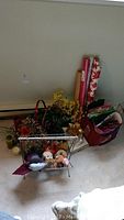 Photo showing metal magazine rack filled with faux plants, toys, wrapping paper rolls, and gift bags on carpeted floor