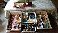 Wide view of the costume jewelry lot showing assorted necklaces, earrings, bangles, wristwatches, jewelry bags, and cases arranged in boxes on table.
