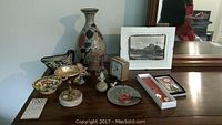 Photo displaying multiple items on a wooden surface including pottery vase, Stangl Pottery bird figurine, metal footed dish, framed print, small clock, magic hanger, and boxed ornaments