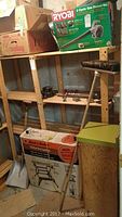 Overall shelf and floor view showing boxed Ryobi blower, boxed Black & Decker Workmate, broom, shovel, clamps.