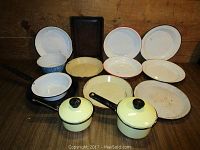 Photo showing vintage enamelware including pie plates, bowls, frying pan, baking dish, and small pots arranged on wooden surface.
