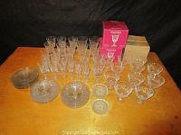 Wide view of entire set on wooden surface including cups, plates, coasters, and two unopened boxes of Pinwheel crystal glasses.