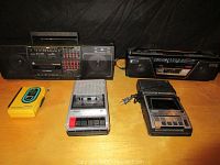 Lot of 5 cassette players on wooden surface including two boomboxes and three portable units.