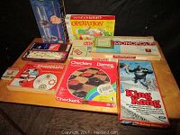 Wide shot showing all 9 board games on a table including Monopoly, Operation, Kerplunk, Checkers, King Kong, Spirograph and others.