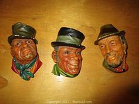 Three chalkware Bossons heads arranged on a wooden surface, showing full front views of each piece.