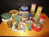 View of assorted vintage kitchen tins in multiple shapes and sizes arranged on a wooden surface with black background.