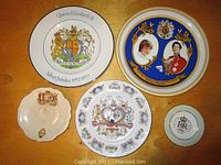 Five decorative plates displayed on a wooden surface, featuring royal family commemorative themes including Queen Elizabeth II Silver Jubilee and Prince Charles and Lady Diana Spencer wedding.