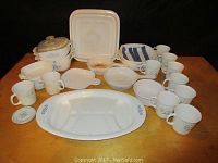 Wide view of Corningware set including platters, casserole dishes, mugs, and bowls arranged on wooden surface.