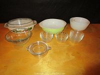 Full set of vintage Pyrex items including white and green bowl, white mixing bowls, clear glass covered dish with floral design, clear glass bowl, three clear glass ramekins, and small covered dish with handles.