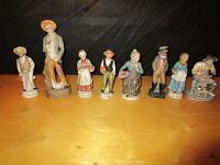Eight porcelain figurines in a row on a wooden surface against a black background, showing various characters, some elderly and rural workers.