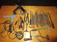 Full layout of vintage hand tools on a wooden surface showing a mix of files, screwdrivers, brace, propane heat gun, and auto tools