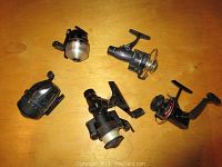 Five fishing reels laid out on a wooden surface, showing different sizes and designs.