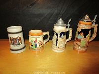Four German beer steins displayed in a line showing variety in size and design, two with lids and two without.