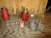 Four vintage glass decanters, six brandy glasses, colorful vintage bar stir sticks in red container, six swirl-patterned glasses on metal stand, and a music box decanter container.