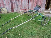 Full view of vintage green Pennsbury harness racing sulky on grass in front of weathered wooden door.