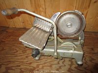 Front side view of the vintage meat slicer showing the circular slicing blade, lever arm with wooden handle, and metal carriage.