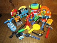 Full assortment of boys toys displayed on wooden background including colorful trucks, cars, construction vehicles, play tools, and a space football toy.