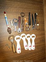 Top-down photo of 12 assorted bottle openers showing various styles, brands and handle types including wooden and plastic handles, guitar shape, bullet shaped, and metal designs.