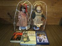 Two Anne of Green Gables dolls with dust covers and three Anne of Green Gables books on a wooden surface.