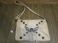 Front view of beige leather purse with skull and wings decoration and metal studs.