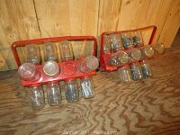 Two vintage red metal nail holders with multiple clear glass jars filled with assorted nails and fasteners, placed on wooden floor.