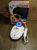 White Tide Buzz ultrasonic stain remover device with attached handheld wand, on wooden surface with original box behind