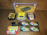 Two portable Discman CD players, one cassette player/recorder, six Fuji blank cassette tapes, MP3 Doctor LCD repair kit, and earphones displayed on a wooden surface.