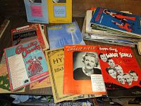 Large pile of vintage/antique sheet music with various colorful covers including war songs and holiday themes.